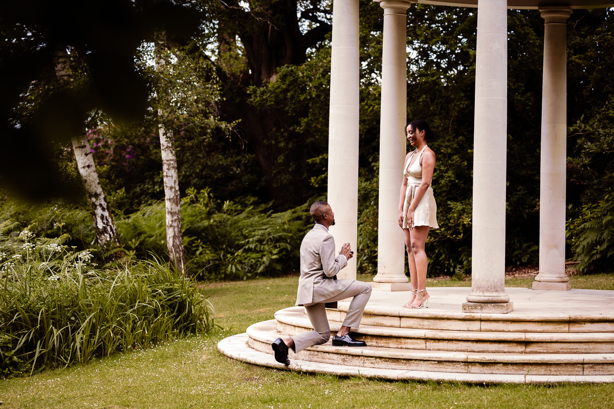 young black man kneels on steps to a pavillion yo propose to a young black girl at Lower lake Heckfield Place