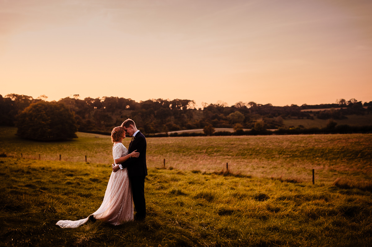 A bride & groom embracing in the fields surrounding Combe Gibbet at sunset