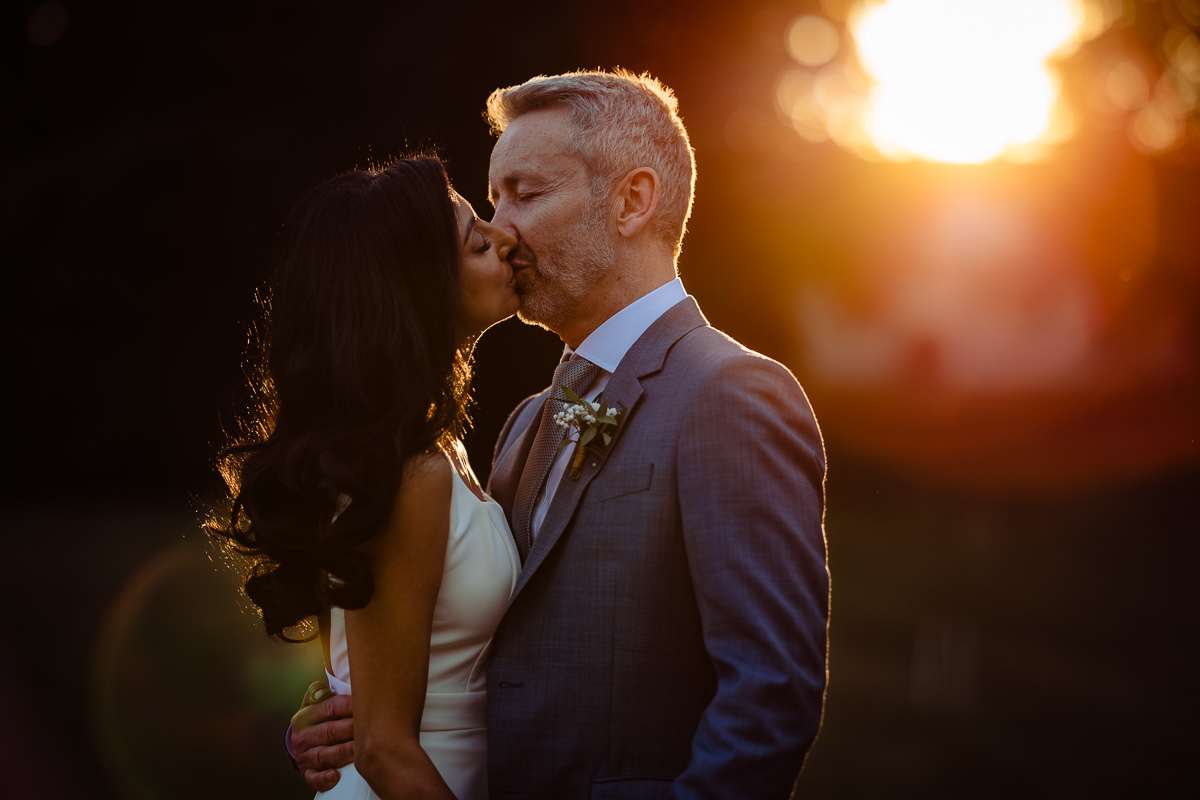 A close up photo of a couple kissing in front of a golden sun flare