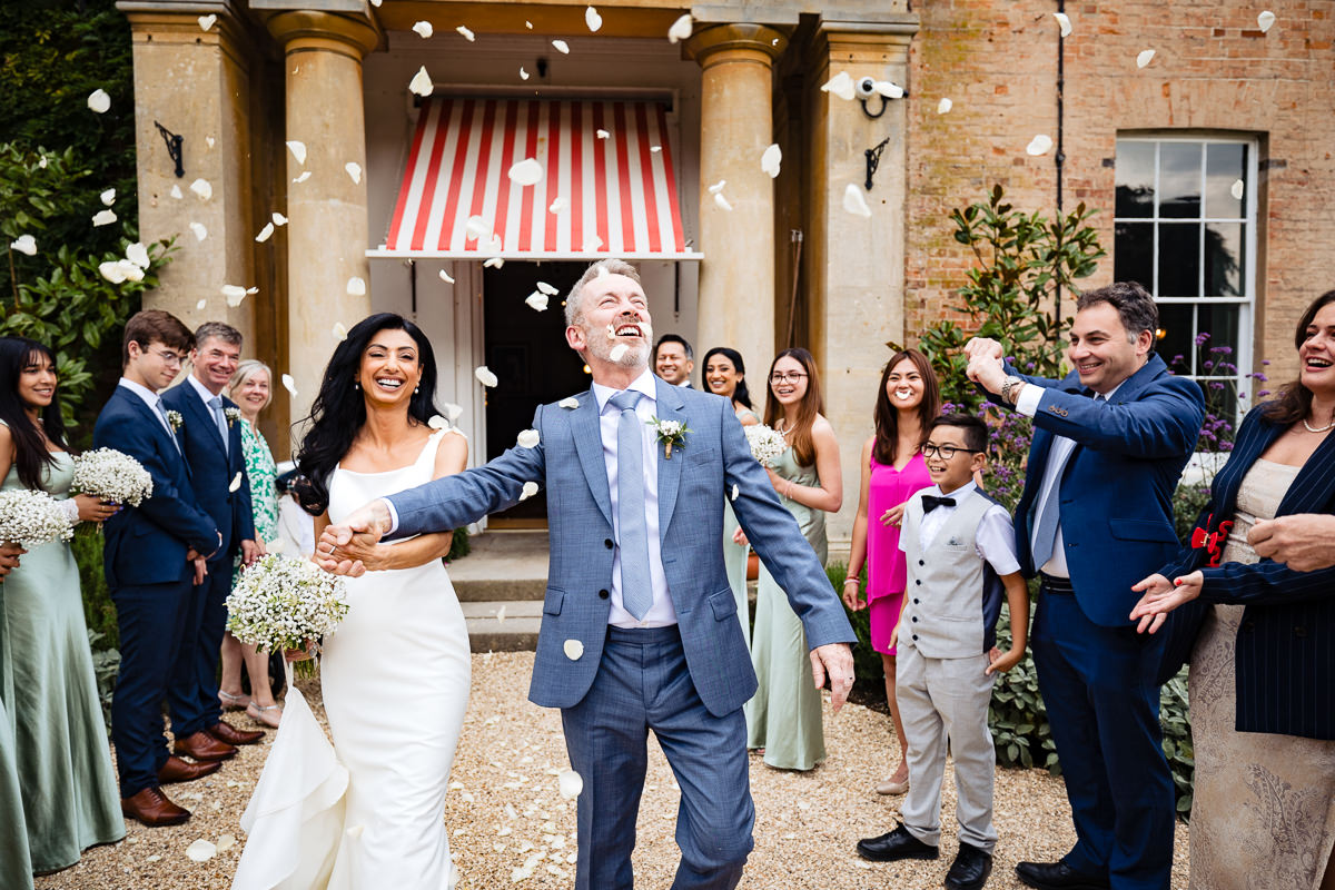 Bride & groom walking through a confetti shower in front of The Retreat at Elcot Park