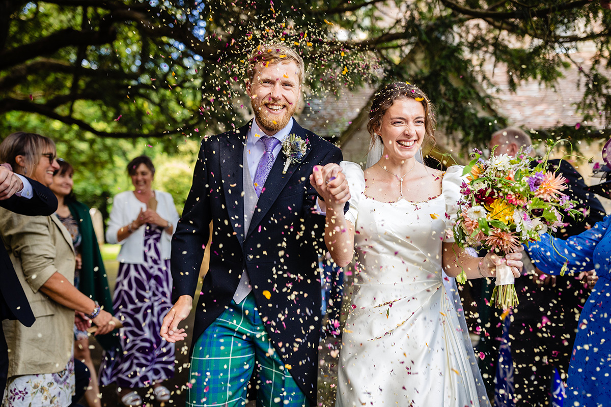 bride & groom hand in hand smiling through a confetti storm