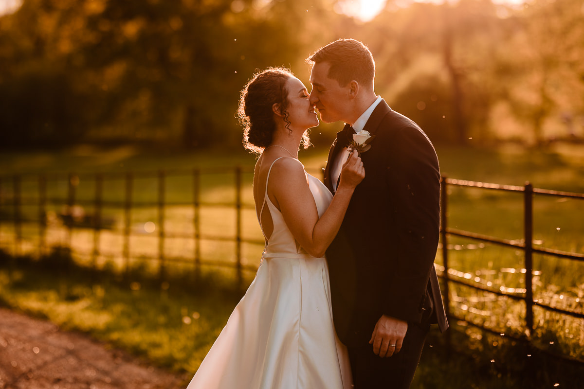 Bride & groom enjoying a quiet moment together during golden hour at Stanlake vineyard. The shy groom is wearing a black tuxedo & the bride a thin strappy backless white satin wedding dress