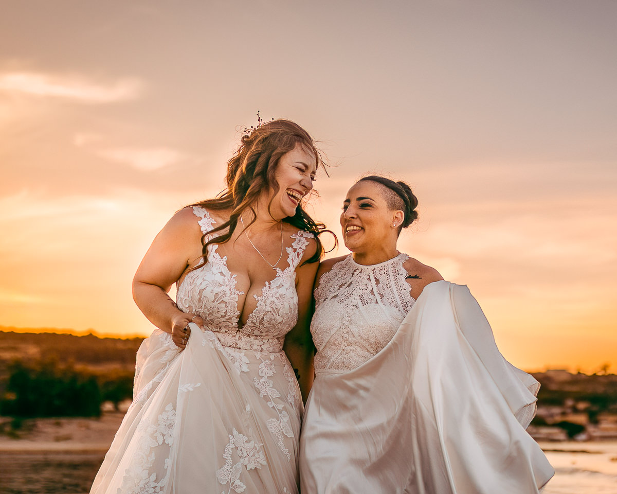 A close up photograph of two brides who are relaxed & laughing. They are walking towards the camera on Melieha beach, Malta